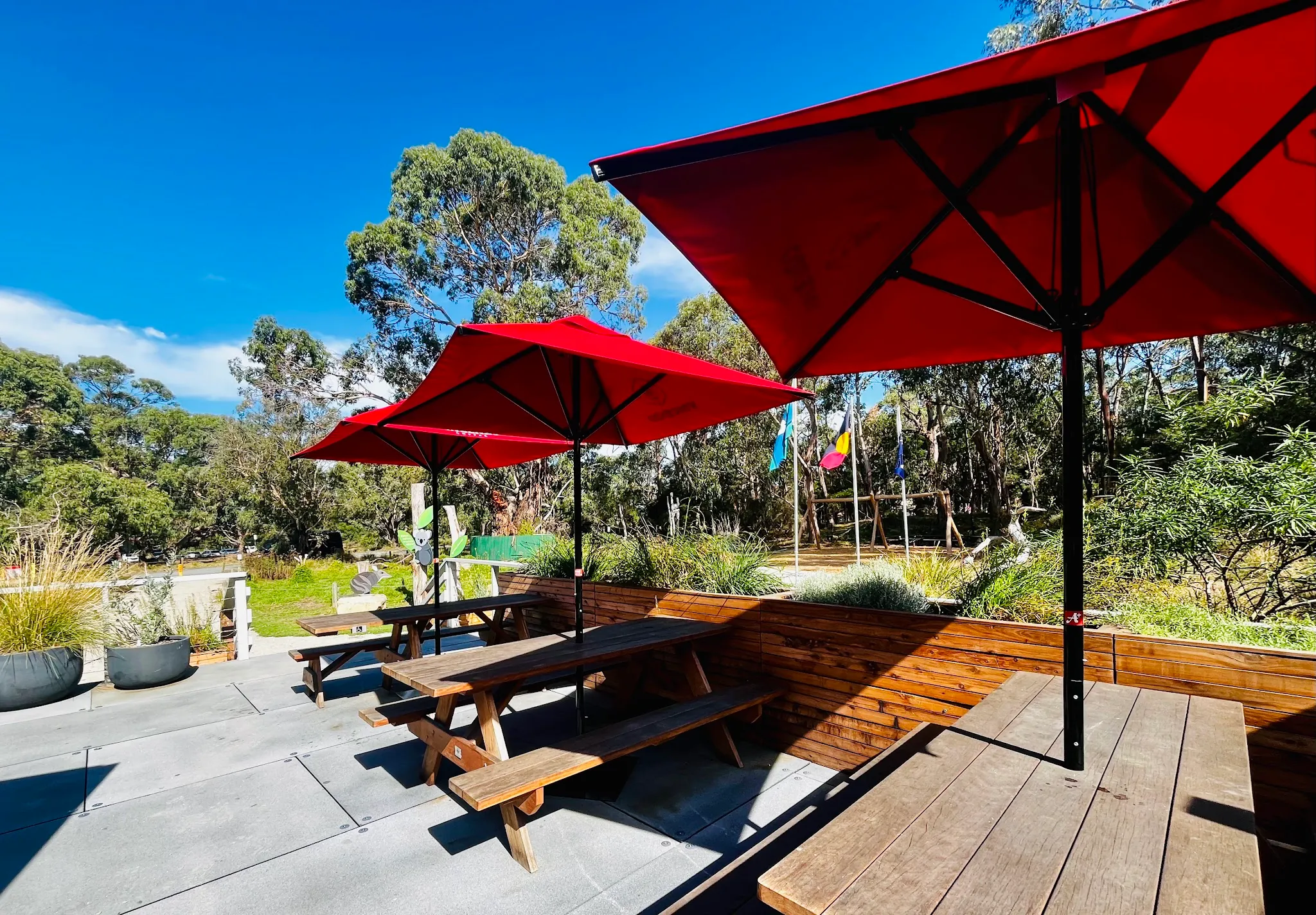 Outdoor cafe deck with red umbrellas and picnic tables surrounded by native Australian bush