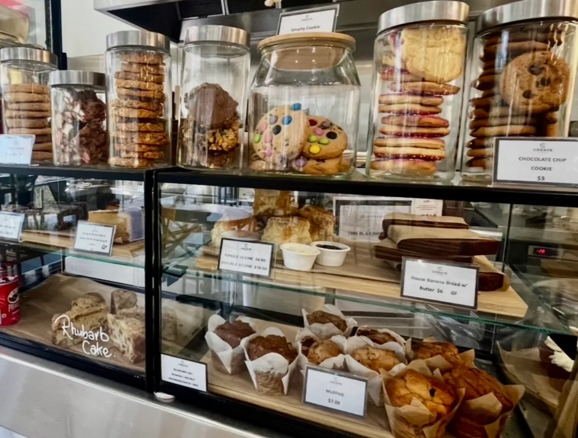 Cafe display cabinet full of cookies, muffins, scones, banana bread, and rhubarb cake with price labels