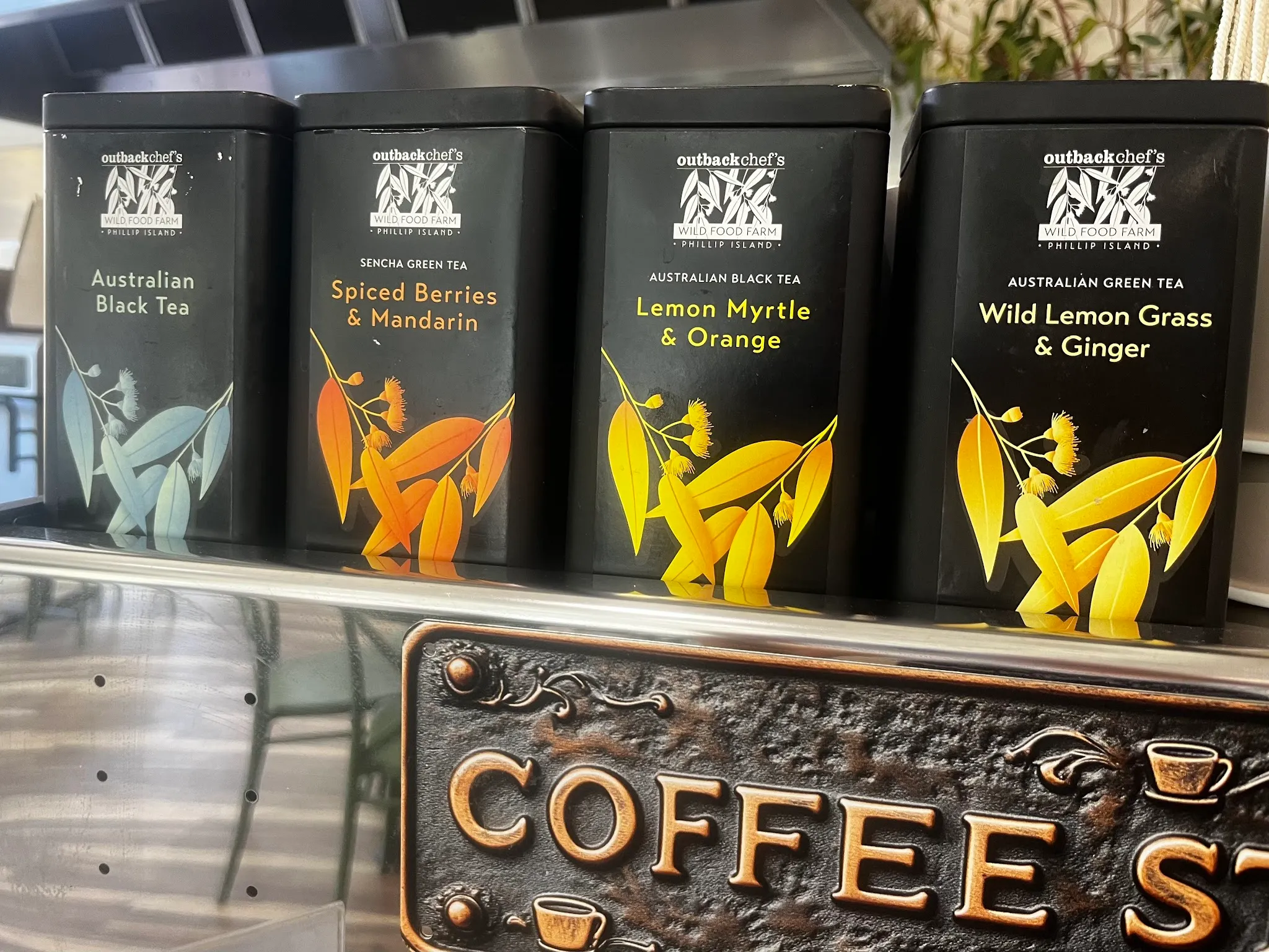 Four Outback Chef Phillip Island tea tins on a shelf above a brass coffee sign